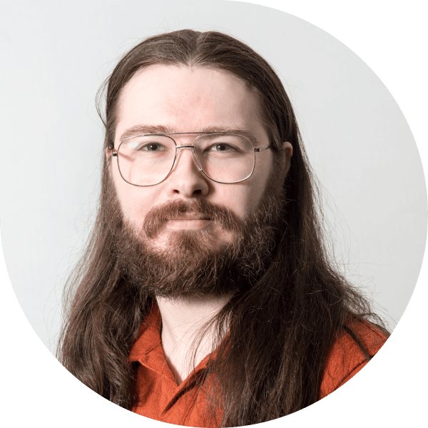 Headshot of Nathan Hughes, Onboarding Team Lead at Fire. He is wearing an orange shirt, thin-framed glasses, a brown beard and moustache, and has his long hair down.