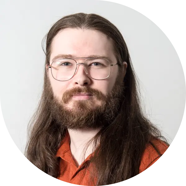 Headshot of Nathan Hughes, Onboarding Team Lead at Fire. He is wearing an orange shirt, thin-framed glasses, a brown beard and moustache, and has his long hair down.