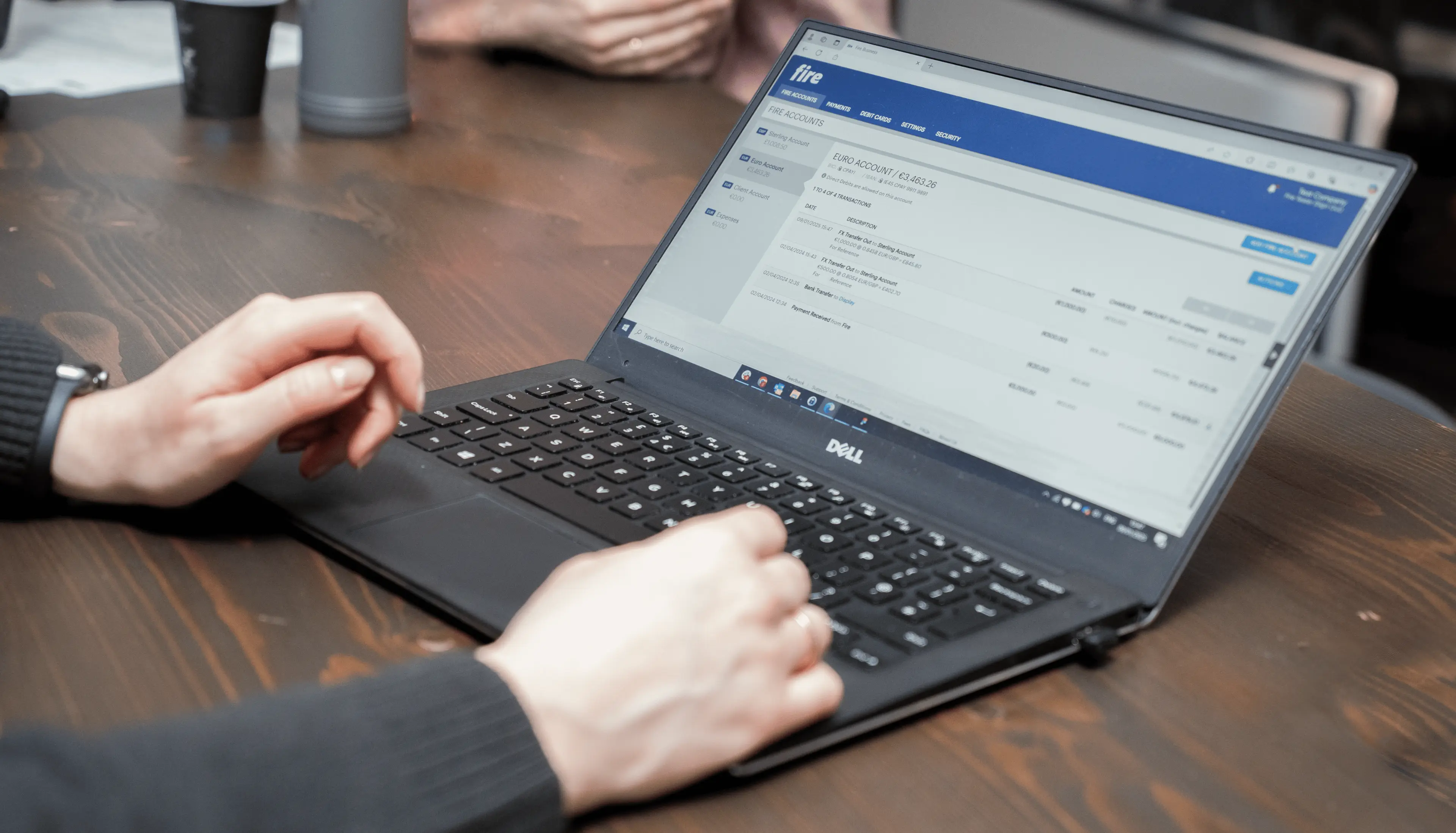 Close-up of hands typing on a laptop keyboard, with a Fire Business account displayed on the screen. The laptop is placed on a wooden desk.
